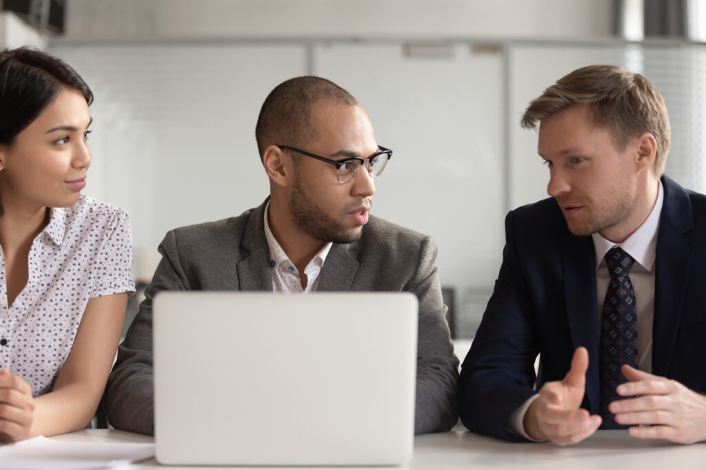 Diverse employees work at laptop discussing project together